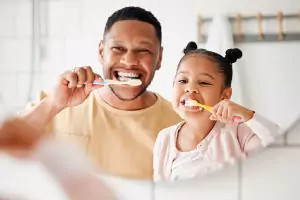 A man and his daughter look in the mirror and brush their teeth after visiting Cottage Dental Care, a Dentist in Normal IL