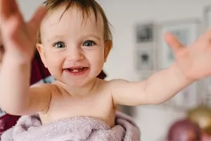 A baby smiles with a mouth full of teeth. A child’s first dentist appointment should happen between age one or within six months after a first tooth appears.